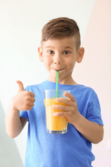 Cute little boy drinking juice on light background