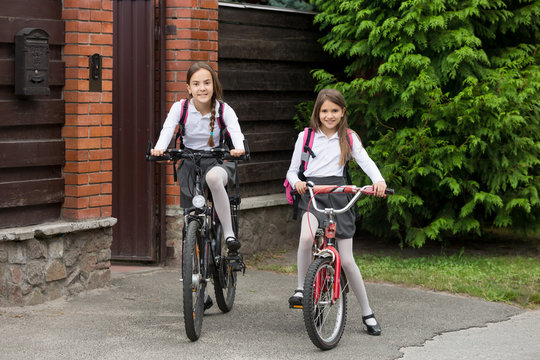 Two happy girls in school uniform riding to school on bicycles