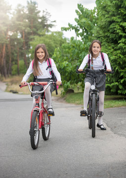 Two beautiful smiling schoolgirls riding to school on bicycles