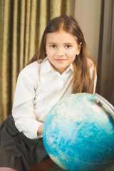 Portrait of smiling schoolgirl posing with Earth globe at cabinet