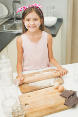 Portrait of smiling girl rolling dough with wooden pin on kitchen