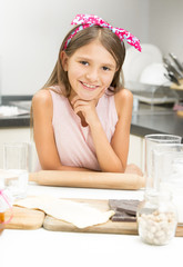 Portrait of cute girl with pink bow on hair posing with wooden rolling pin