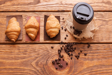 Roasted coffee beans, plastic cup and desserts on wooden background. Closeup of seeds on dark brown cafe table. Top view.