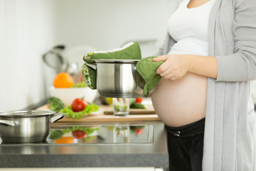 Pregnant woman posing on kitchen while cooking soup