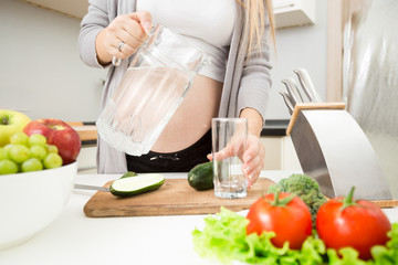 Fototapeta na wymiar Young pregnant woman pouring water in glass on kitchen