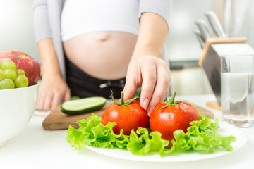 Obraz na płótnie Canvas Young pregnant woman taking fresh tomato from plate