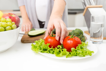 Fototapeta na wymiar Closeup photo of woman picking fresh tomato from table on kitchen