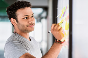 Thoughtful male worker writing ideas on small papers