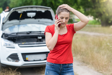 Portrait of sad woman standing at broken car and calling for help