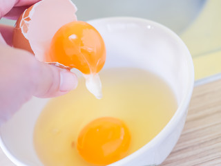 Closeup of hand, eggs yolk and egg white in white bowl for cooking
