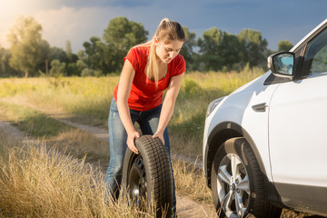 Young woman rolling spare tire to change the flat one