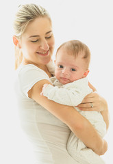 Smiling caring mother cuddling her 3 months old baby at big window at sunny day