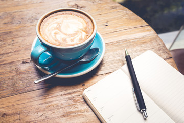 Cup of coffee latte with notepad top view on wooden table/vintage