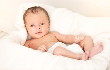Smiling baby boy lying on soft beige blanket and cushion