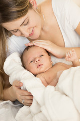 Closeup portrait of young caring mother hugging newborn baby on bed