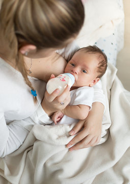 Closeup portrait of young mother feeding baby with milk from bottle