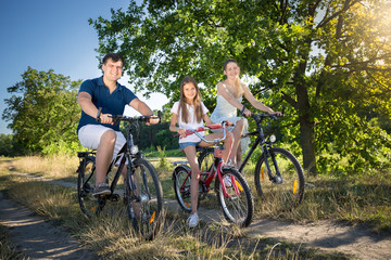 Obraz premium Young parents riding on bicycles with their daughter at park