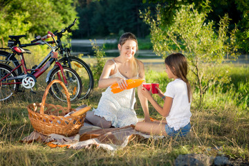 Happy mother and daughter drinking orange juice at picnic