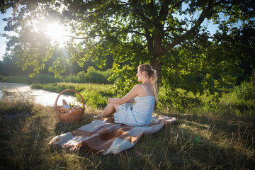 Beautiful woman relaxing on blanket under tree and looking at sunset
