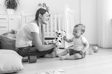 Black and white image of beautiful young mother and her 10 months old baby son playing with puppets...