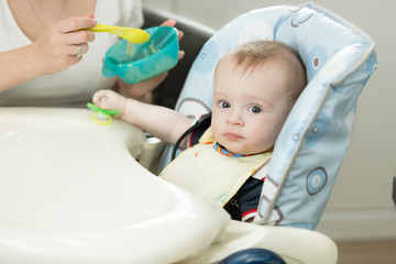 Cute little boy sitting in highchair at kitchen