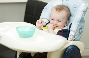 Baby boy sitting in highchair and playing with spoon and dish