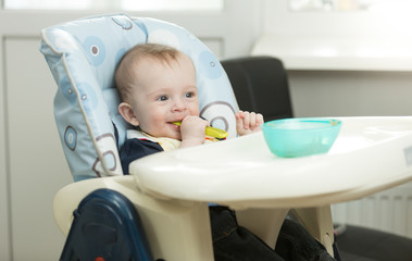 Baby boy siting in highchair on kitchen and eating