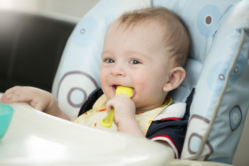 Beautiful 9 month baby boy playing with spoon while eating
