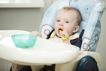 Cheerful smiling baby boy playing with spoon in highchair