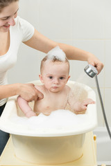 Cute baby boy playing in bath with shower head