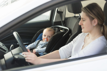 Woman driving car with baby sitting on front seat