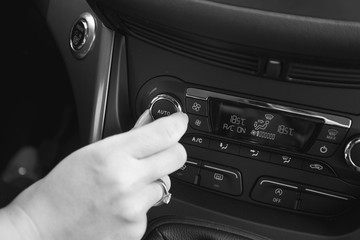 Black and white image of hand adjusting car air conditioner temperature