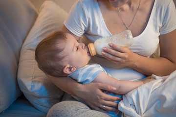 Portrait of beautiful baby boy drinking milk from bottle at night