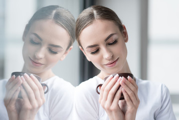 Jolly young beautiful woman drinking hot beverage at home