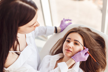 Top view of a woman a client lies on the procedure for eyebrow correction. Young women tweezing her eyebrows in beauty salon.