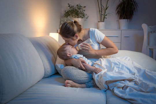 Young Mother Feeding Her Baby From Bottle In Bed At Night