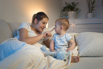 Young mother playing with baby son on bed at night