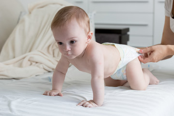 9 months old baby boy in diapers crawling on bed