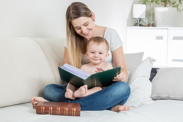 Young mother reading book to her smiling baby boy