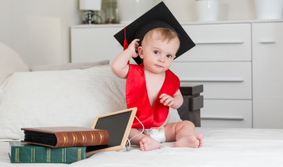 Funny baby boy in black graduation cap holding book