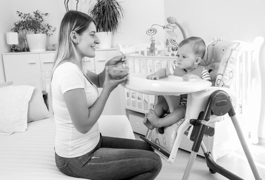 Monochrome image of beautiful young mother feeding her baby boy in highchair