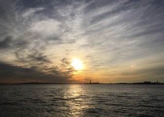 Statue of Liberty on Liberty Island in New York Harbor at Sunset. Dramatic sky with dynamic clouds at sunset. Statue of Liberty in the distance surrounded by water at sunset. Liberty island at sunset.