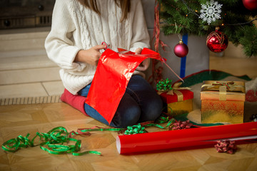 Closeup image of girl wrapping presents under Christmas tree