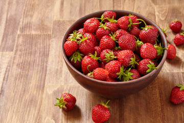 Fresh red strawberries in a brown clay bowl on wooden table.