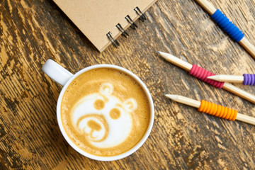 Coffee cup and pencils. Bear latte art, top view.