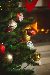 Closeup image of baubles hanging on Christmas tree on background of burning fireplace
