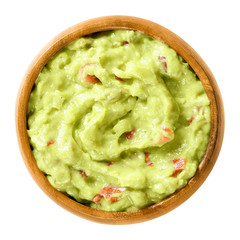 Guacamole in wooden bowl. Also short guac, a light green dip or salad, made of mashed avocados, tomatoes, onions, garlic, lemon, cayenne pepper and salt. Macro food photo close up on white background.
