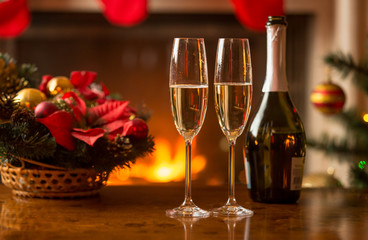 Closeup of glasses of champagne on table next to old clock showing midnight at living room decorated for Christmas