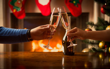 Male and female hands clinking with glasses of champagne at living room decorated for Christmas