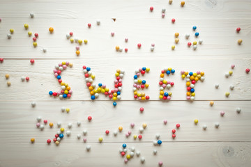 Word Sweet written by little colorful candies on white wooden background